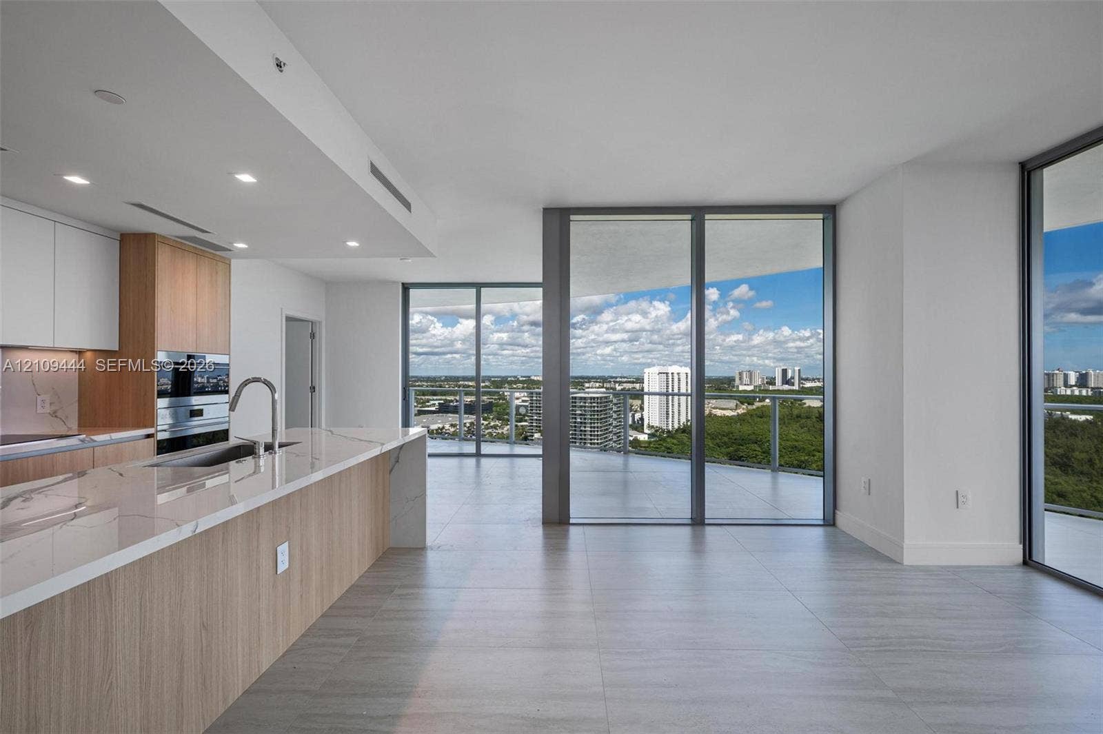 Kitchen featuring wood-finish cabinetry, stone countertops, built-in double ovens, and expansive floor-to-ceiling glass panel doors opening to a wrap-around balcony with exterior horizon scenery