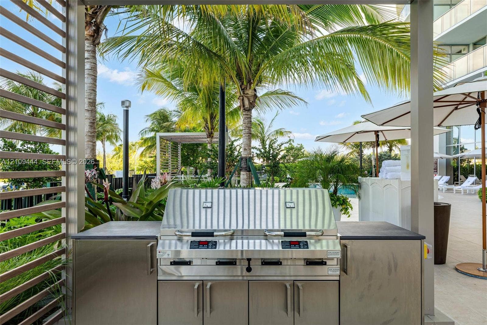 Outdoor kitchen featuring stainless steel cabinetry, a built-in dual-zone grill, and a smooth countertop, sheltered by a metal pergola frame