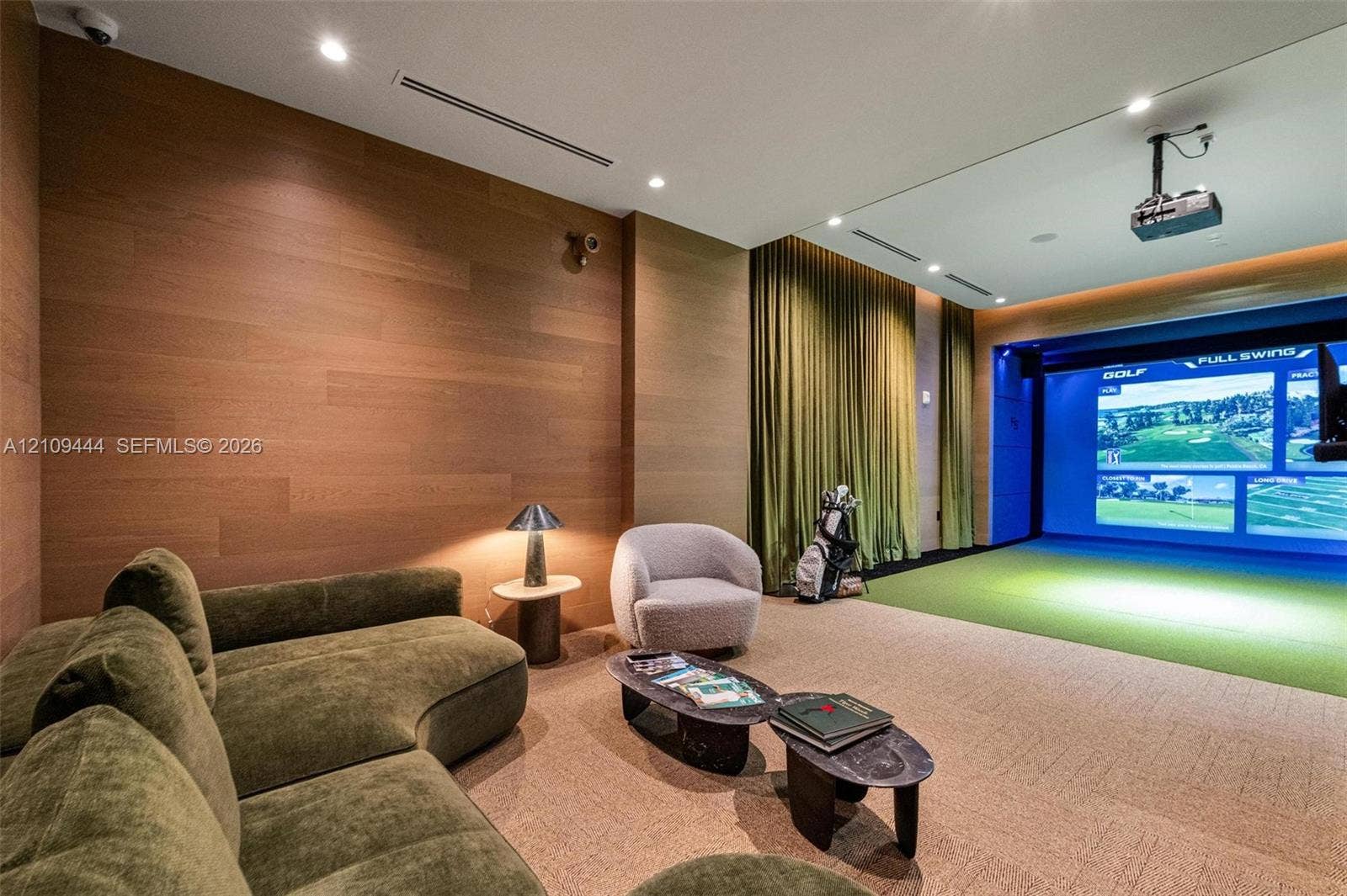 Wood-paneled accent wall, built-in projector system, integrated golf simulator screen, recessed ceiling lighting, and wall-to-wall carpeting
