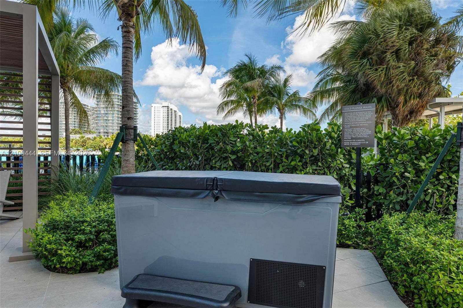 Outdoor hot tub featuring a hard-top cover and integrated step, set on a paved patio with a modern pergola and lush perimeter landscaping