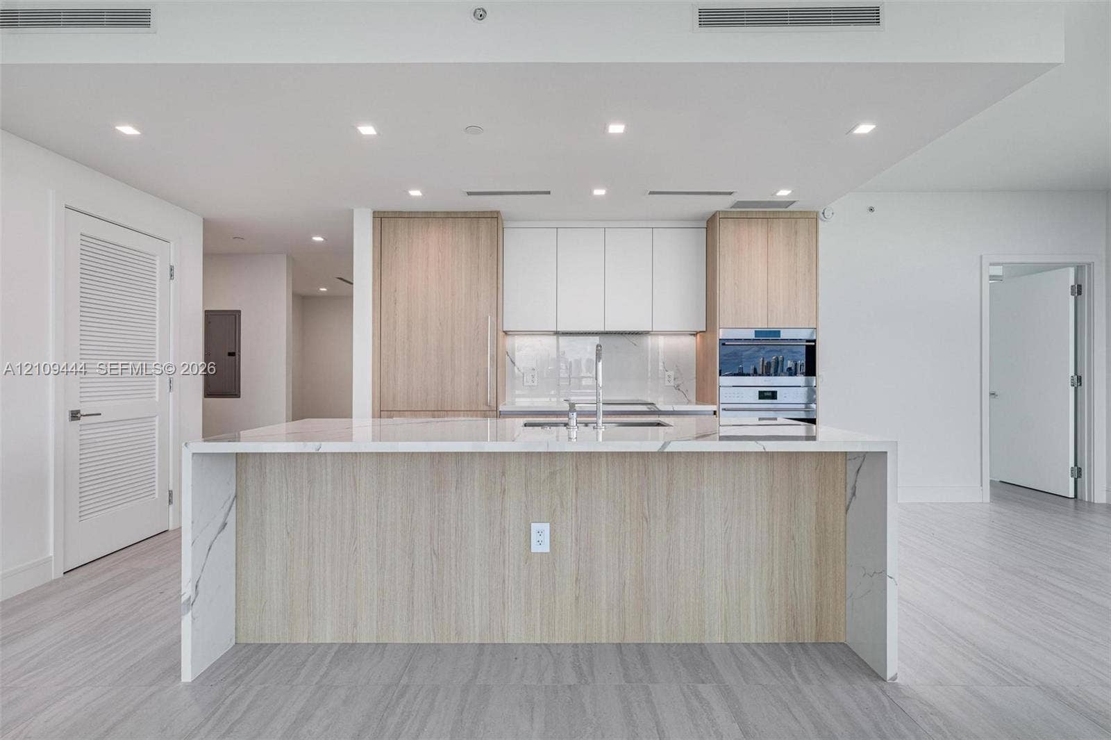 Kitchen featuring a center island with a stone-finish waterfall countertop, custom wood-finish cabinetry, white matte upper cabinets, integrated stainless steel appliances, and neutral flooring