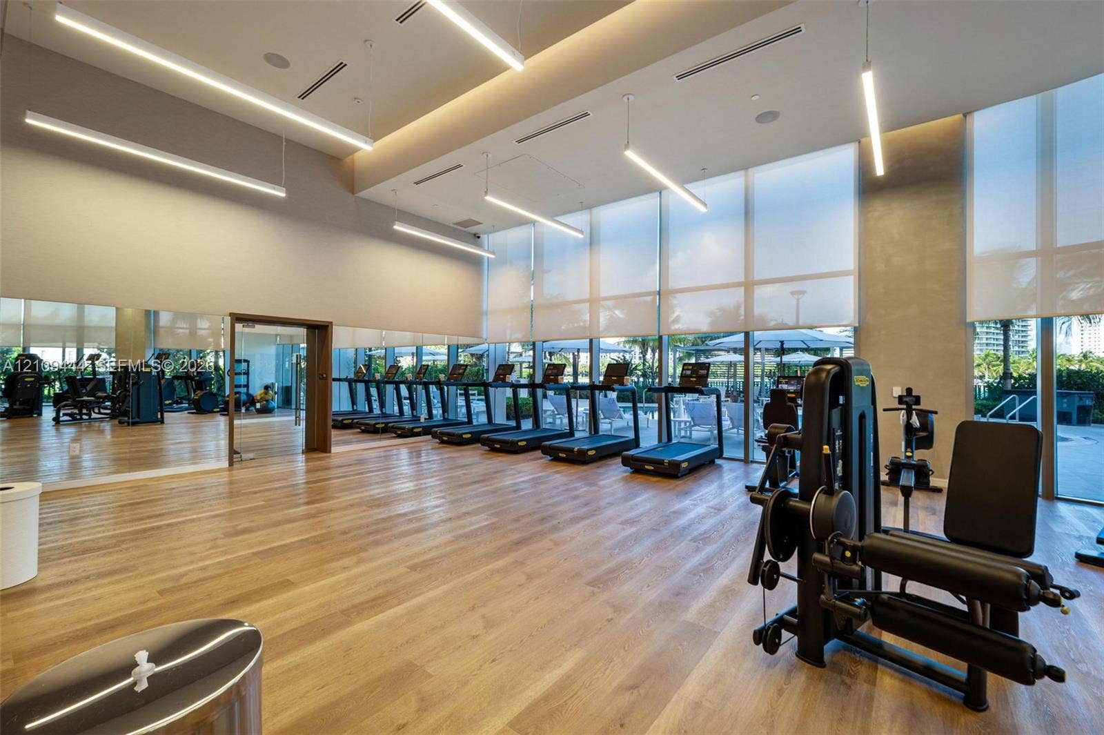 Fitness center featuring wood-finish flooring, floor-to-ceiling windows with roller shades, linear LED lighting, and full-length wall mirrors