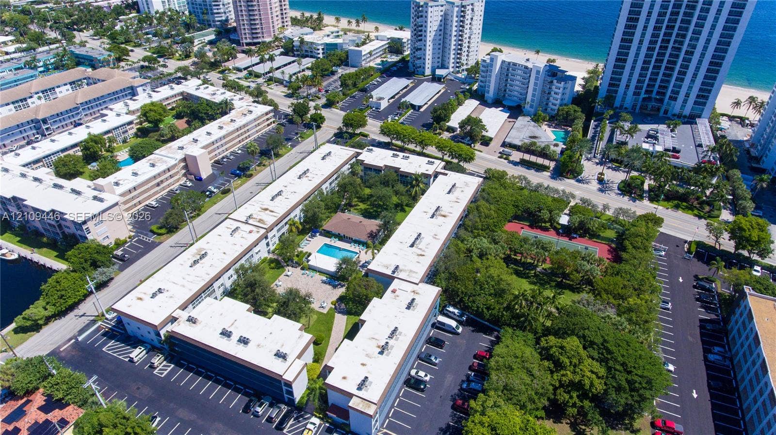 1501 S Ocean Boulevard, #117, Lauderdale-By-The-Sea, Lauderdale By The Sea, FL 33062 Aerial perspective of a multi-building residential complex featuring a central swimming pool, paved surface parking, mature landscaping, and a tennis court
