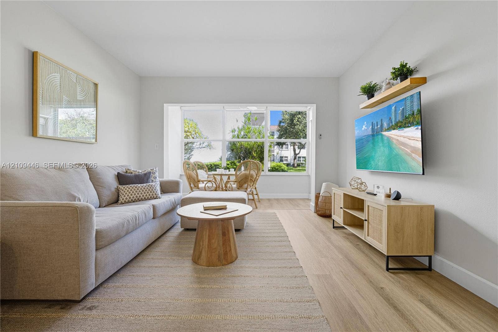 1501 S Ocean Boulevard, #117, Lauderdale-By-The-Sea, Lauderdale By The Sea, FL 33062 Living area featuring wood-finish flooring, neutral walls, large picture window with exterior greenery, and a wall-mounted floating shelf