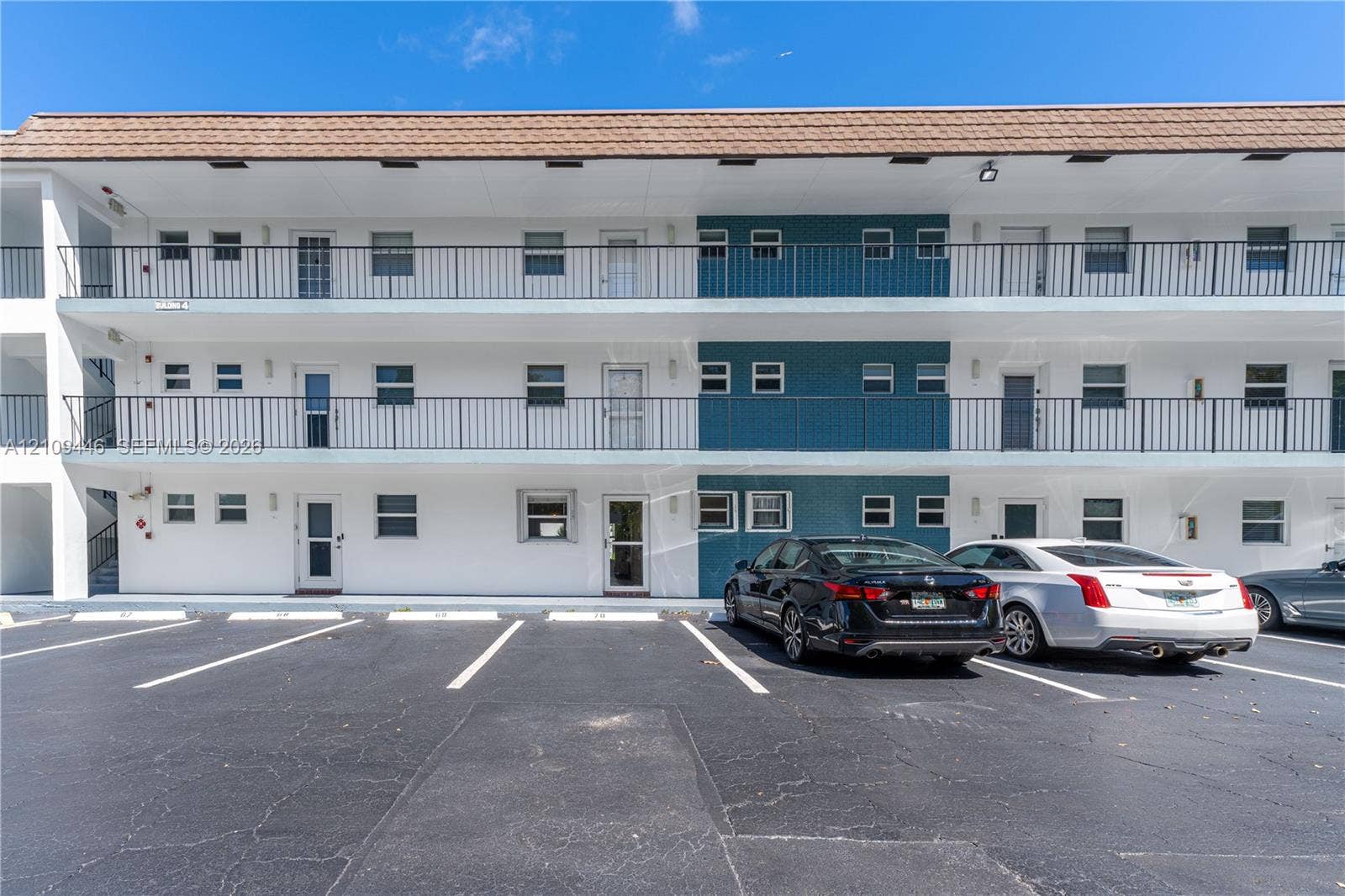 1501 S Ocean Boulevard, #117, Lauderdale-By-The-Sea, Lauderdale By The Sea, FL 33062 Multi-story exterior featuring white stucco siding, blue tile accents, metal balcony railings, and a tiled roof, complemented by a paved parking area
