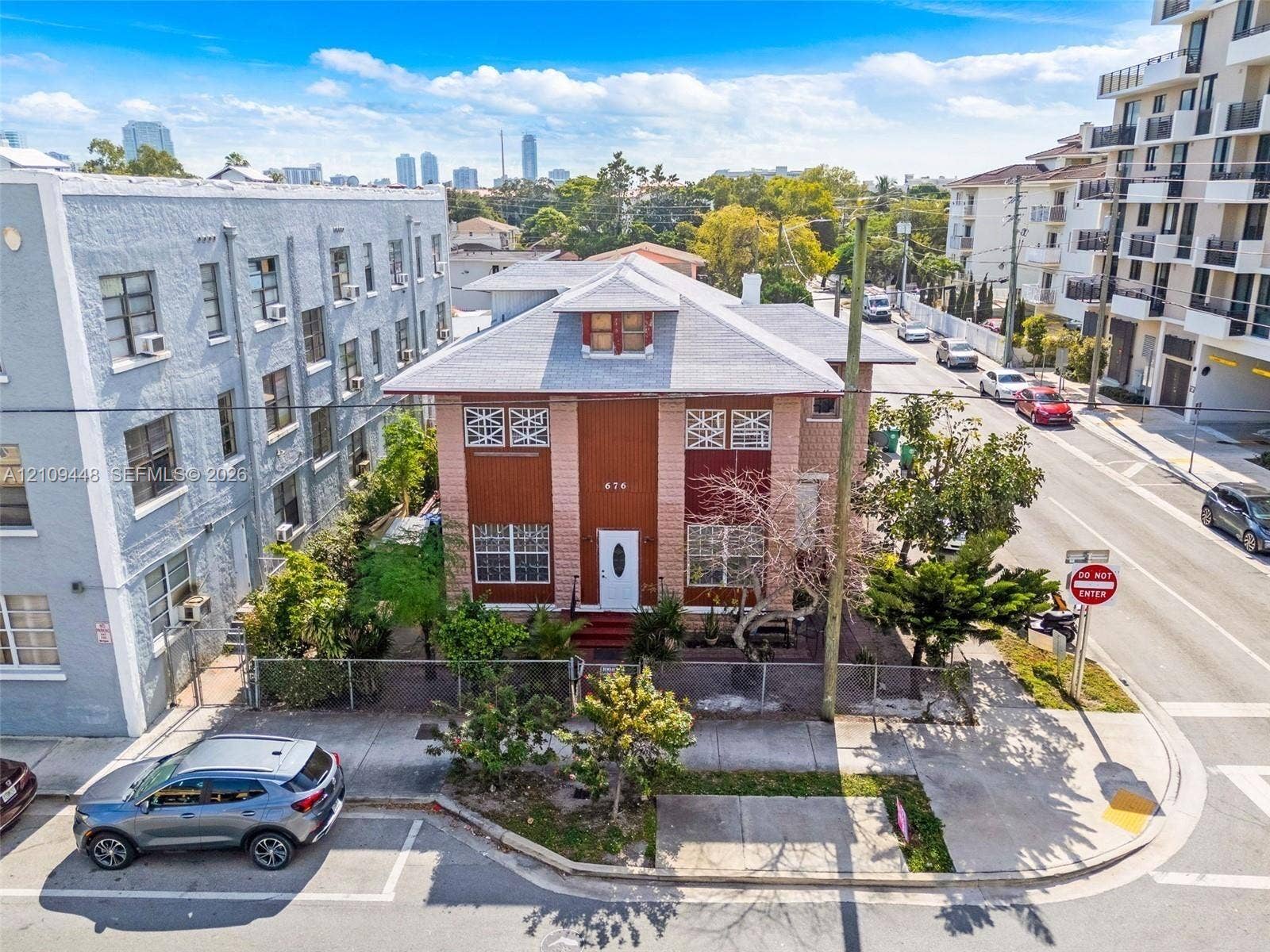 676 SW 1st Street, Miami, FL 33130 Two-story multi-family structure with a hipped roof, dormer window, masonry facade, and perimeter chain-link fencing