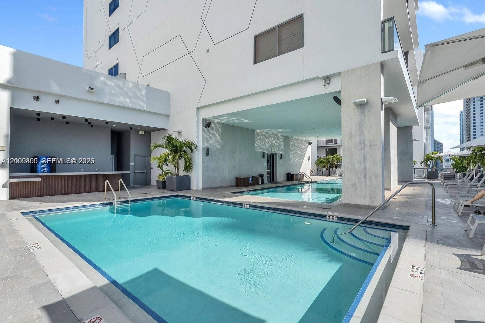 Outdoor swimming pool with integrated stair entry, poolside service bar, concrete decking, and covered patio area