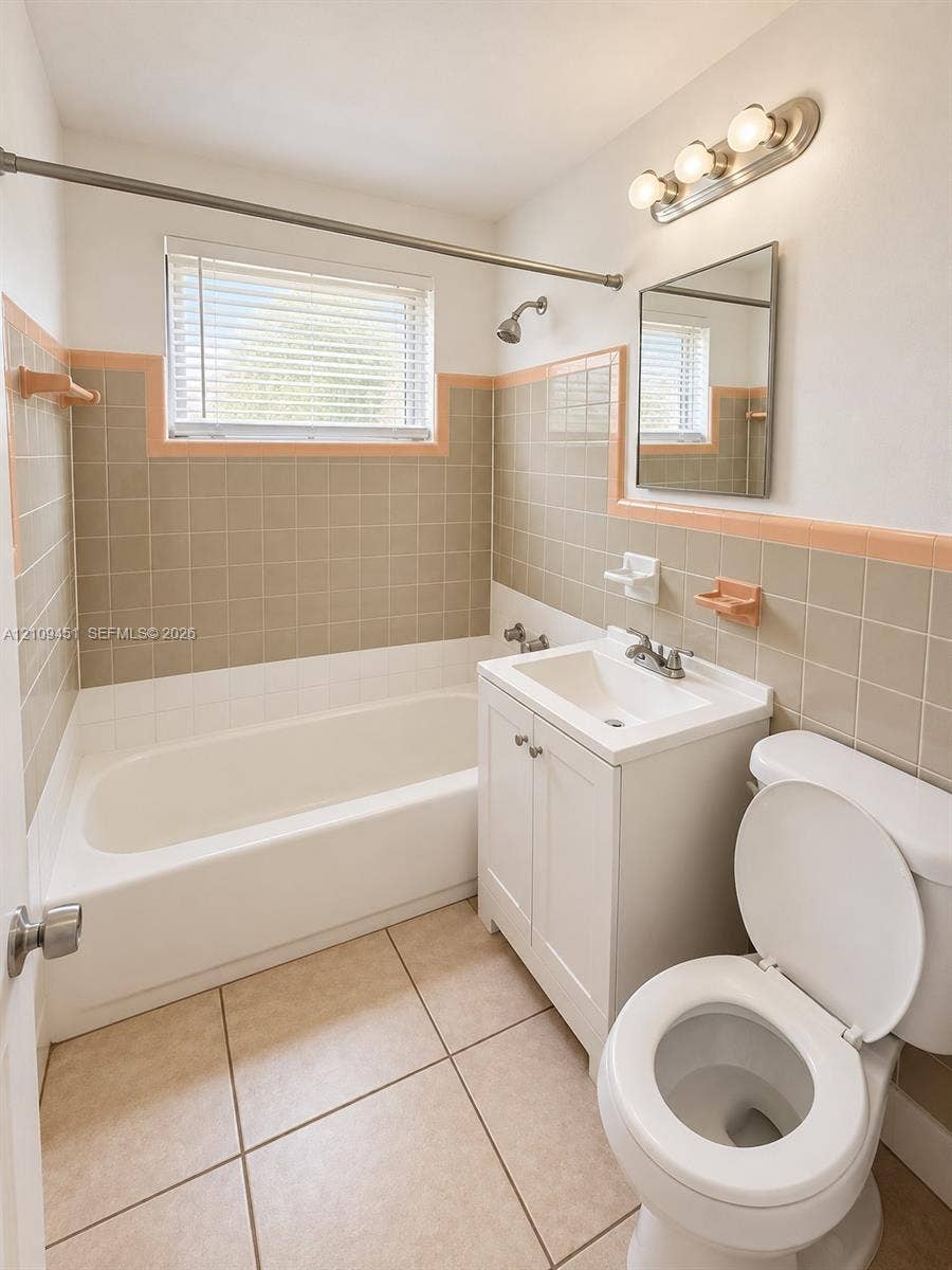 Full bathroom featuring a white vanity cabinet with a ceramic basin, large-format tile flooring, a porcelain bathtub, and wall-mounted tile detailing with accent trim