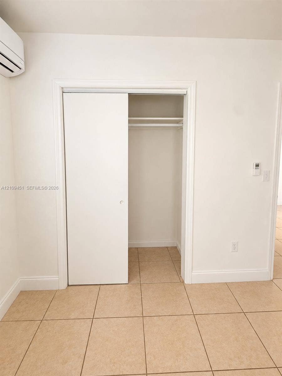 Closet featuring a sliding door and an integrated overhead shelf with hanging rod, accompanied by neutral tile flooring and a wall-mounted climate control unit