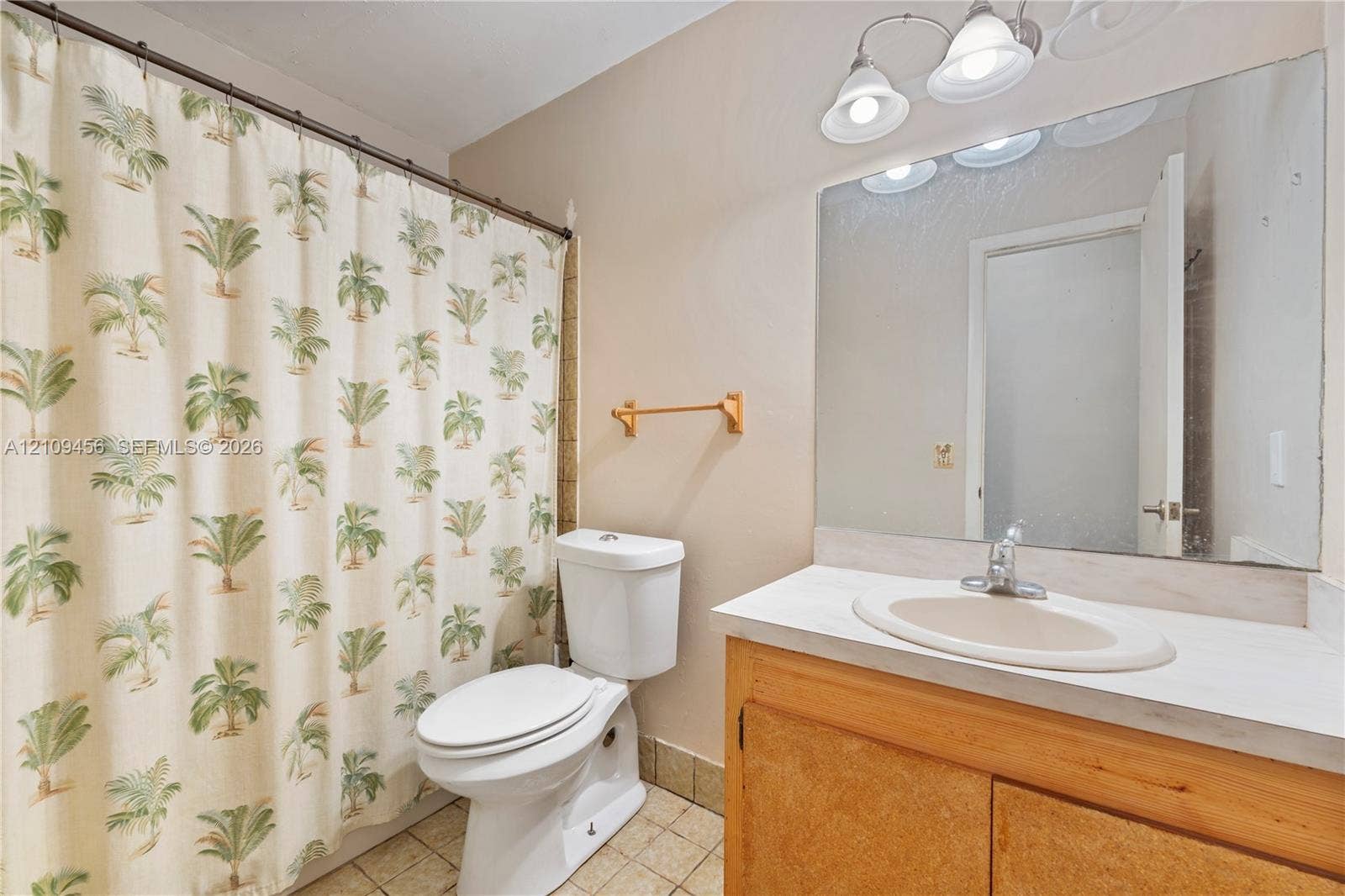 Bathroom featuring a wood-finish vanity with an integrated oval sink, a wall-spanning mirror, three-light vanity fixture, and tiled flooring