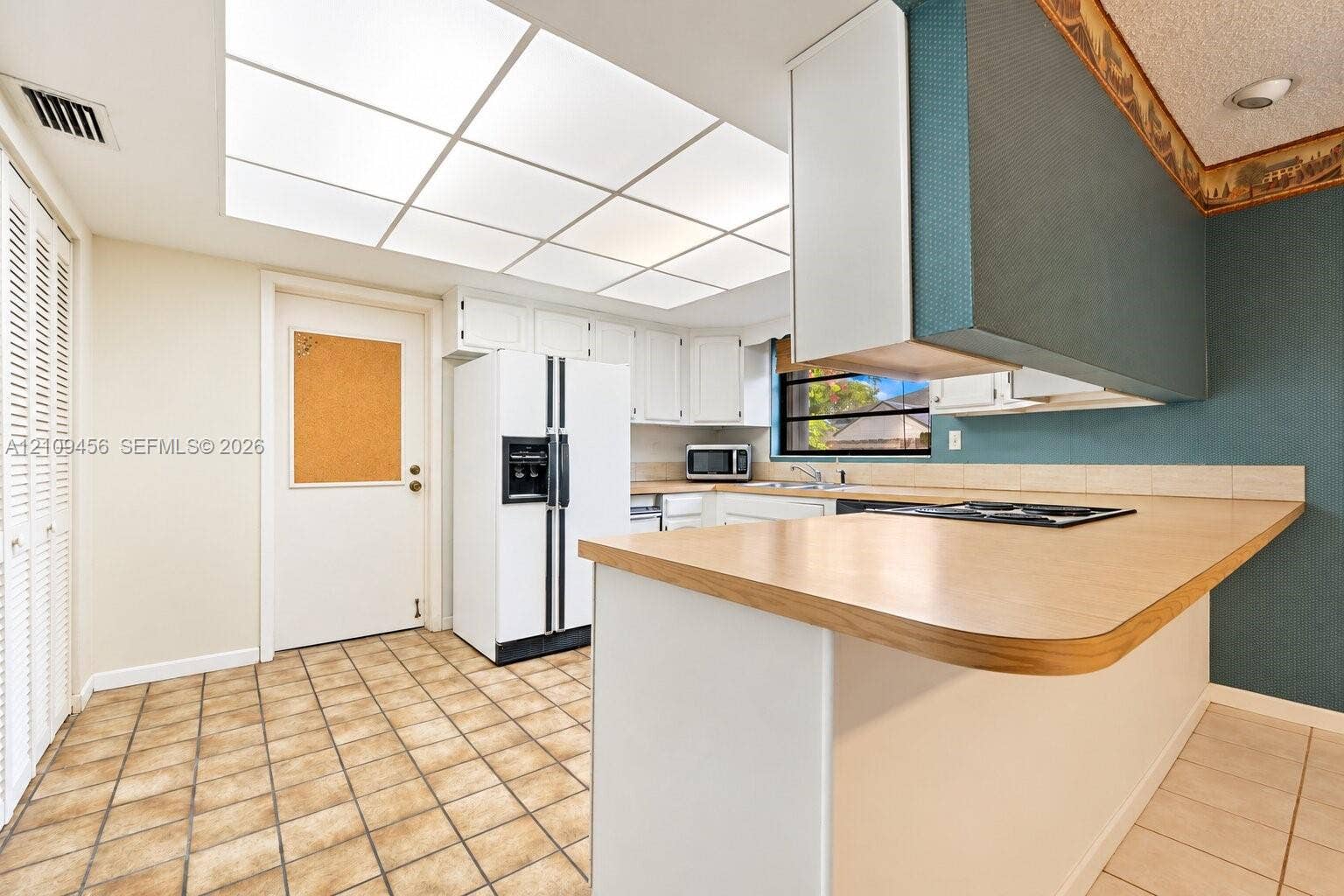 Kitchen featuring a peninsula with laminate countertop, integrated cooktop, white cabinetry, recessed grid lighting, and tile flooring