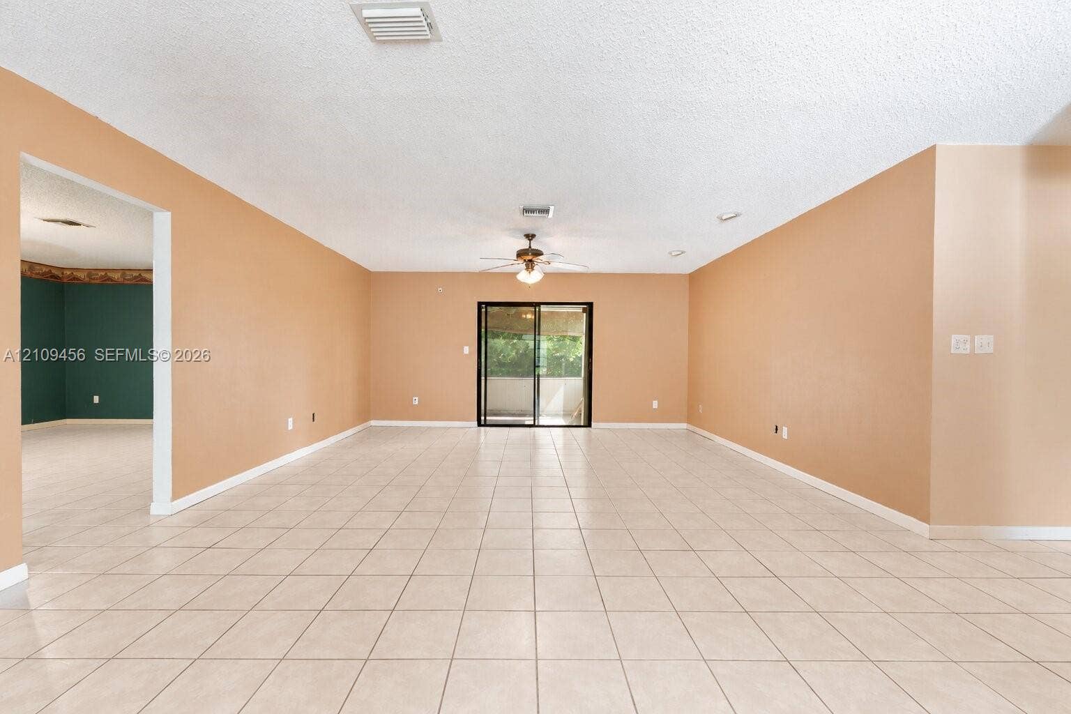 Open-concept interior featuring light-toned tile flooring, neutral wall paint, a ceiling-mounted light fixture with fan, and black-framed sliding glass doors