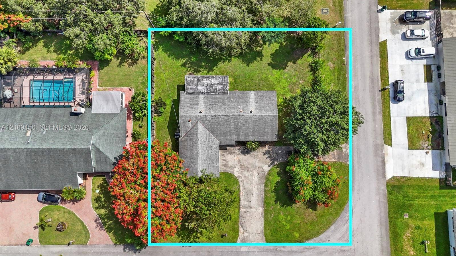 Aerial perspective of property lot featuring an asphalt roof, concrete driveway, mature trees, and expansive lawn area