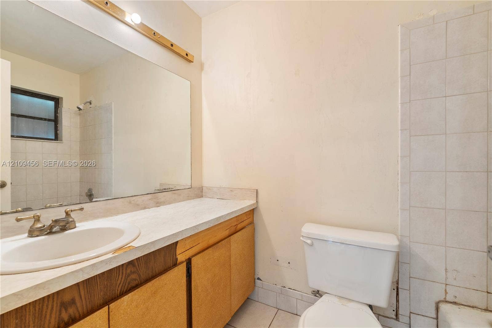 Bathroom featuring a vanity with integrated sink, expansive wall-to-wall mirror, brass-finish hardware, tile-surround tub, and tile flooring