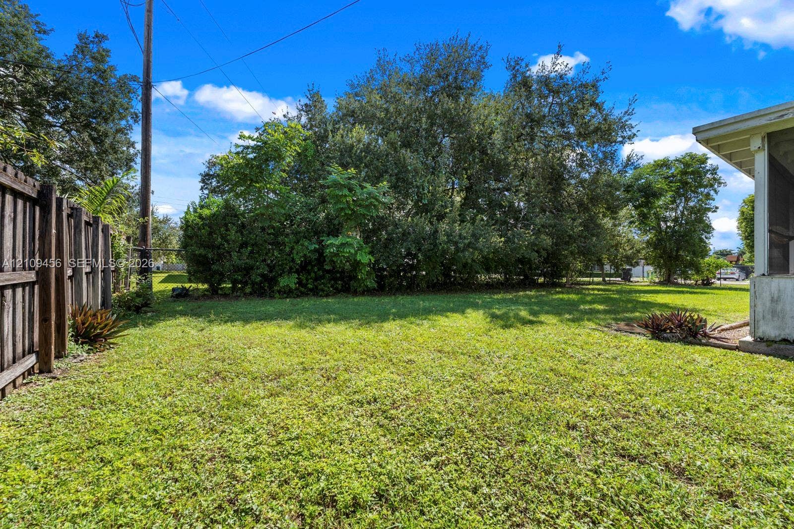 Rear exterior featuring a grass lawn, wooden privacy fencing, and mature trees