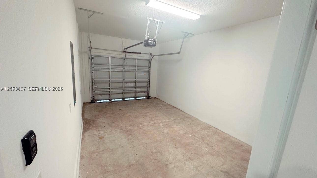 Enclosed single-car garage featuring a roll-up door, automatic overhead opener, fluorescent lighting, and concrete flooring