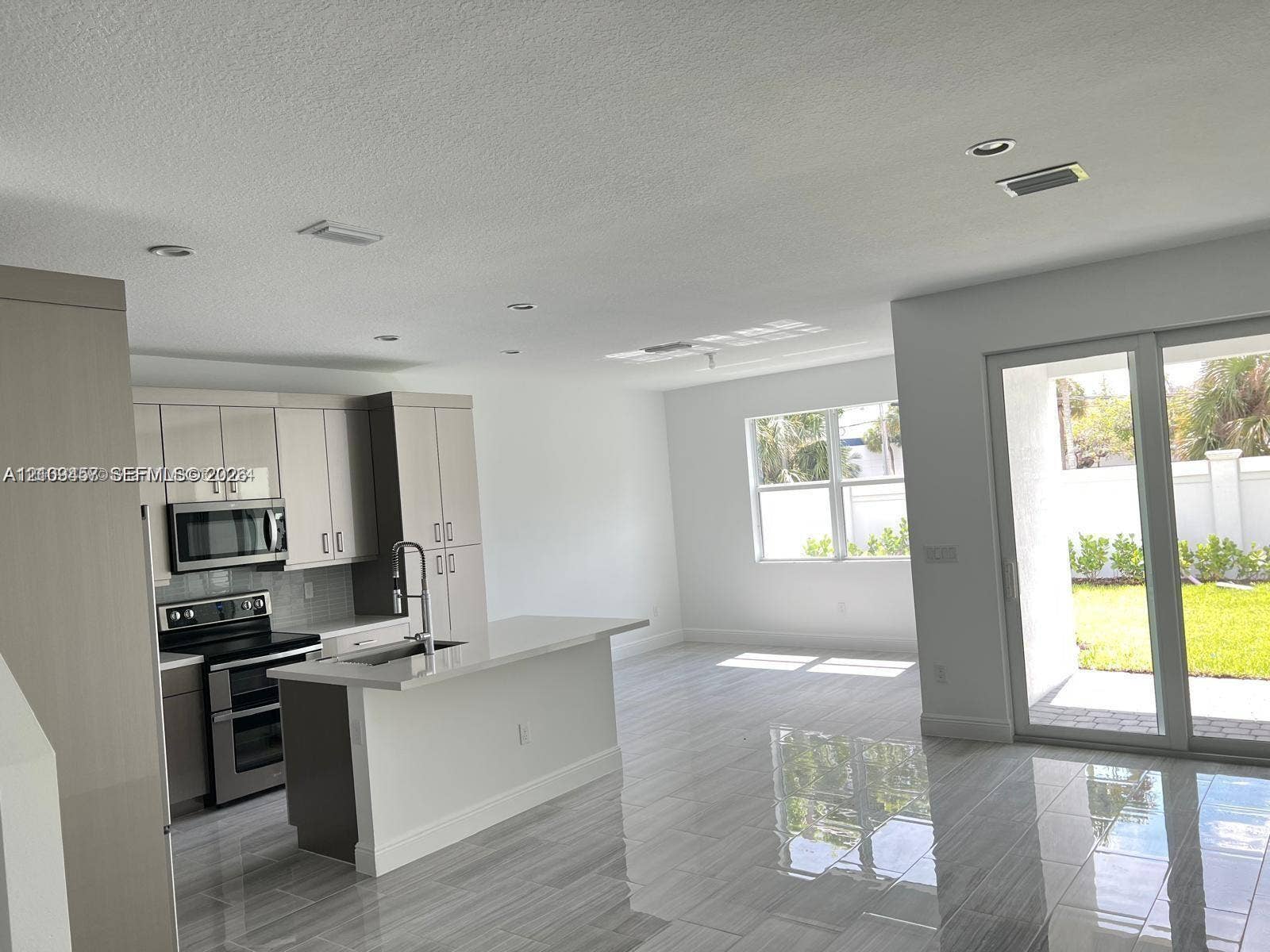 Kitchen featuring flat-panel cabinetry, quartz countertops, a kitchen island with a built-in sink, stainless steel appliances, and large-format porcelain tile flooring