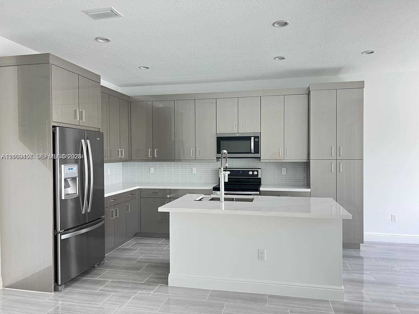 Kitchen featuring high-gloss cabinetry, stone-finish countertops, stainless steel appliances, a central island with a built-in sink, and tile flooring