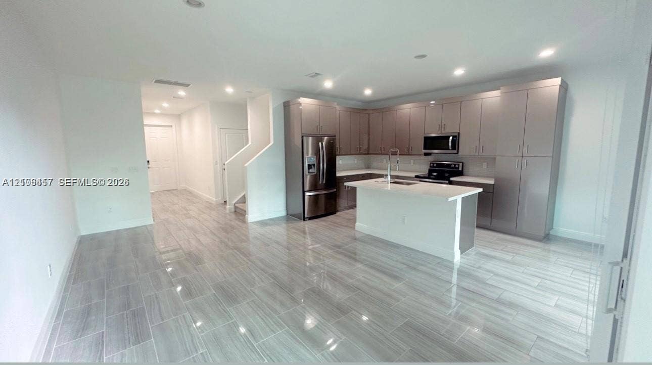 Kitchen featuring high-gloss cabinetry, stone-finish countertops, stainless steel appliances, a central island, and wood-finish flooring throughout the space