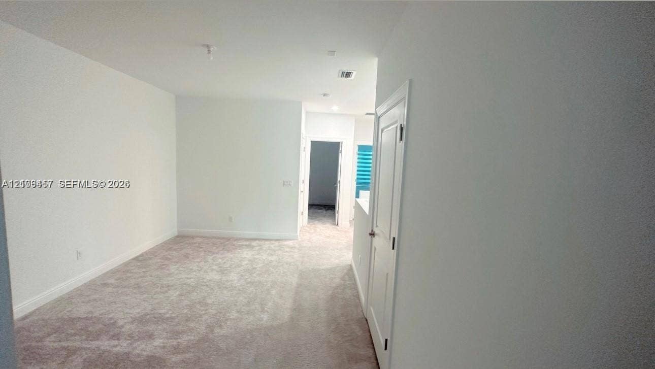 Interior space featuring wall-to-wall carpeting, neutral-tone wall finishes, and a single-panel interior door with brushed metal hardware