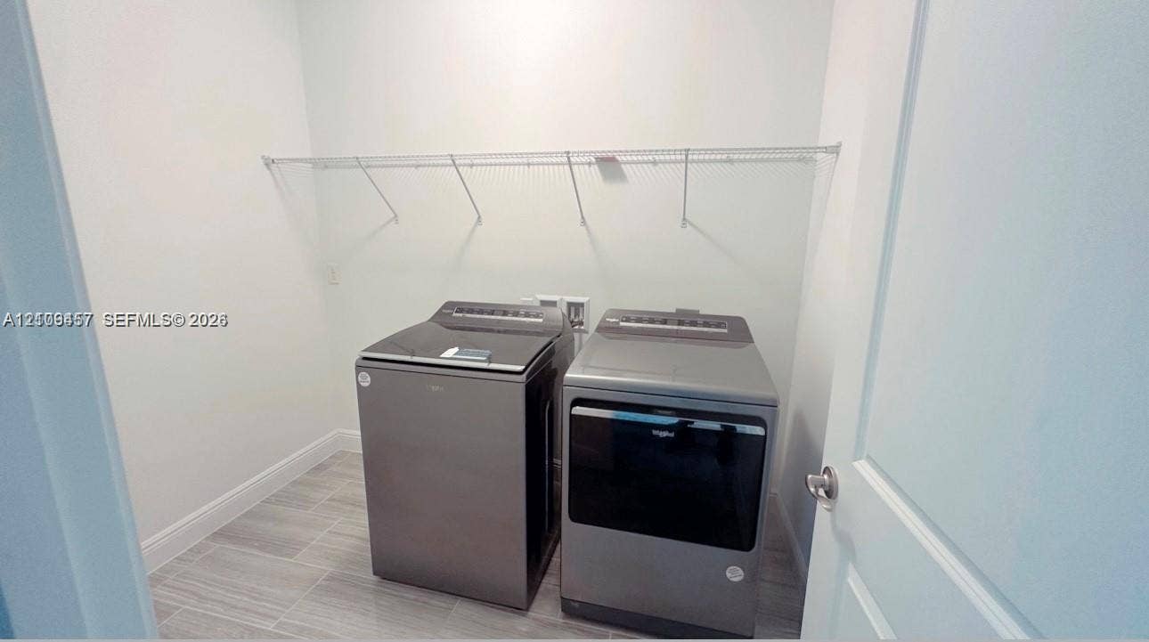 Laundry area featuring grey tile flooring, wall-mounted wire shelving, and built-in washing machine and dryer