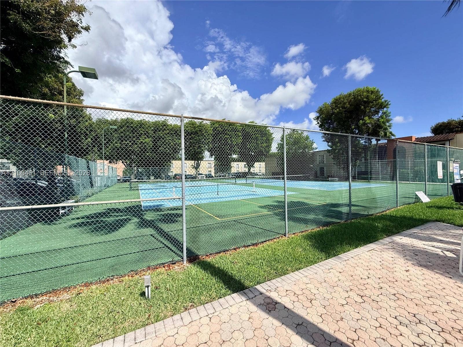 10776 N Kendall Drive, #F11, Miami, FL 33176 Hard-surfaced tennis courts featuring chain-link fencing, dual-tone court surfacing, and interlocking paver walkways