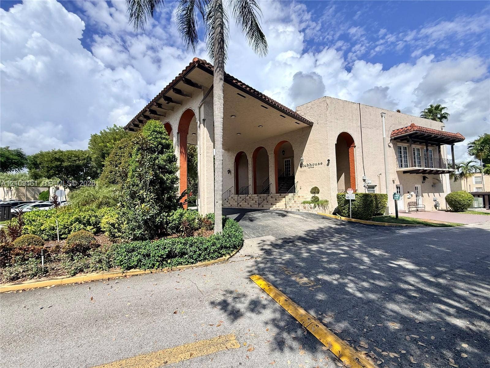 10776 N Kendall Drive, #F11, Miami, FL 33176 Clubhouse exterior featuring a stucco facade, decorative arched columns, tile-accented roofline, and an elevated balcony