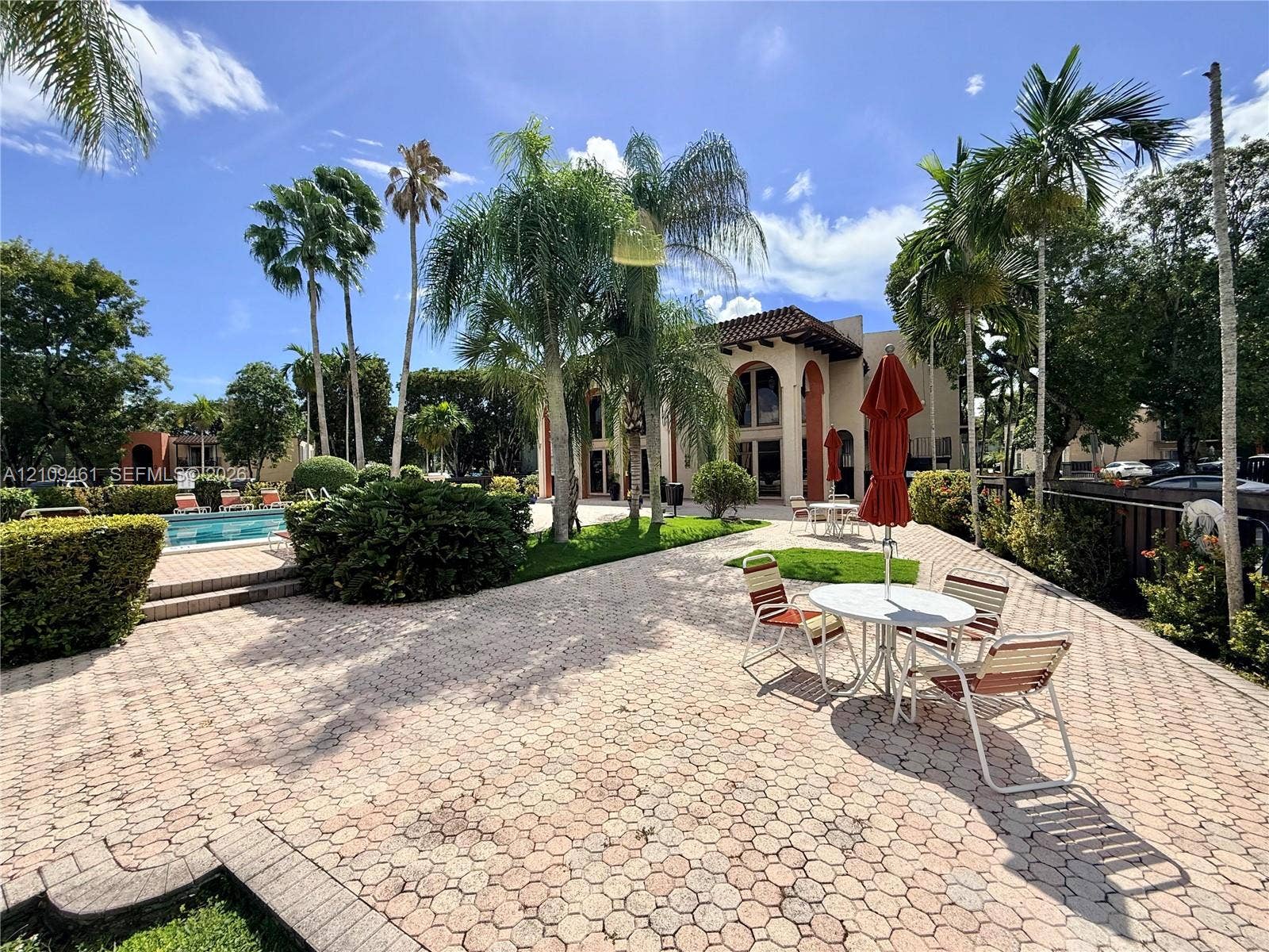 10776 N Kendall Drive, #F11, Miami, FL 33176 Expansive outdoor patio featuring hexagonal paver hardscaping, a swimming pool, mature palm trees, and structural arched architecture