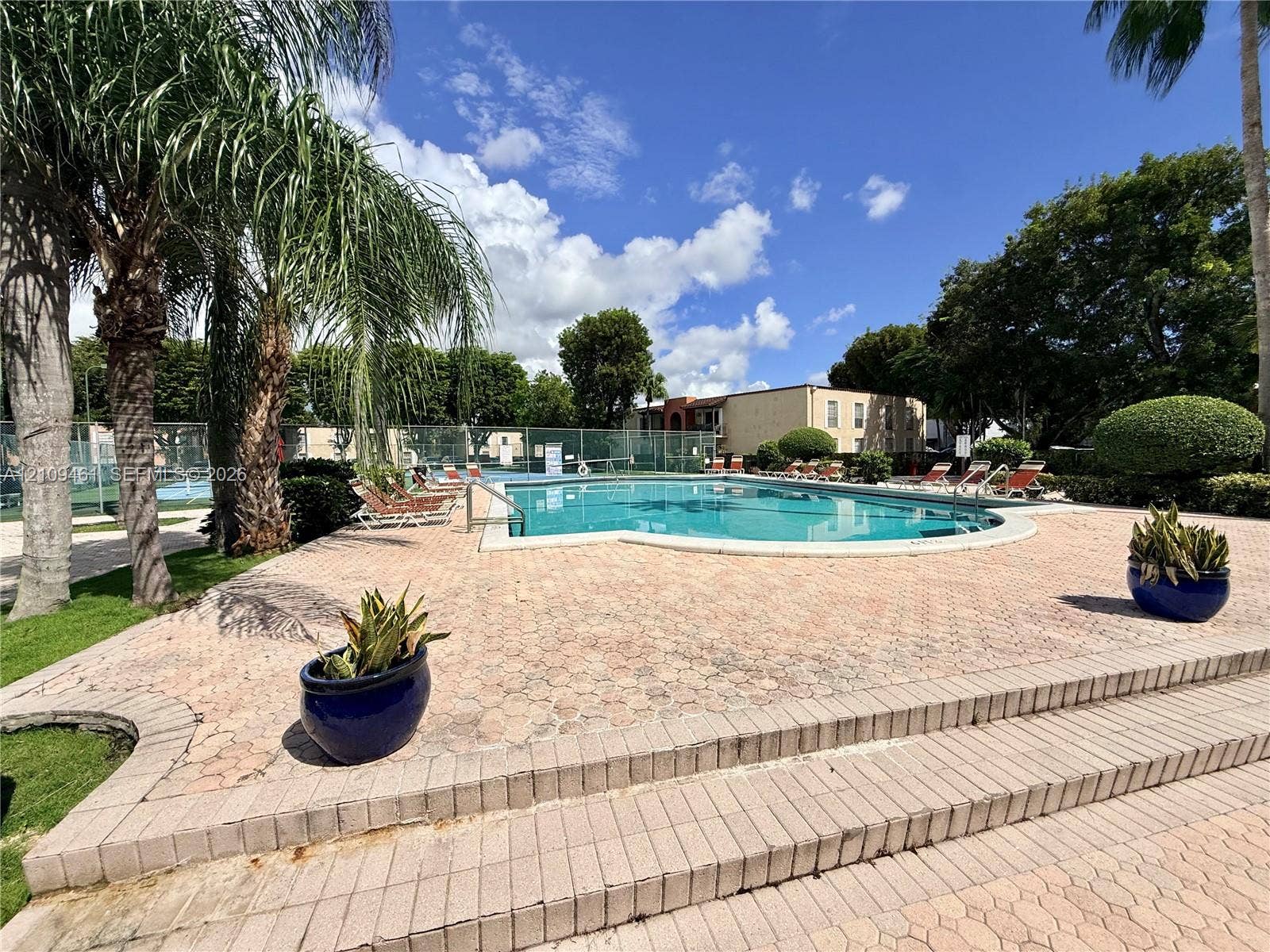 10776 N Kendall Drive, #F11, Miami, FL 33176 In-ground swimming pool featuring a brick-paver deck, tiered stone stairs, perimeter metal fencing, and mature palm trees