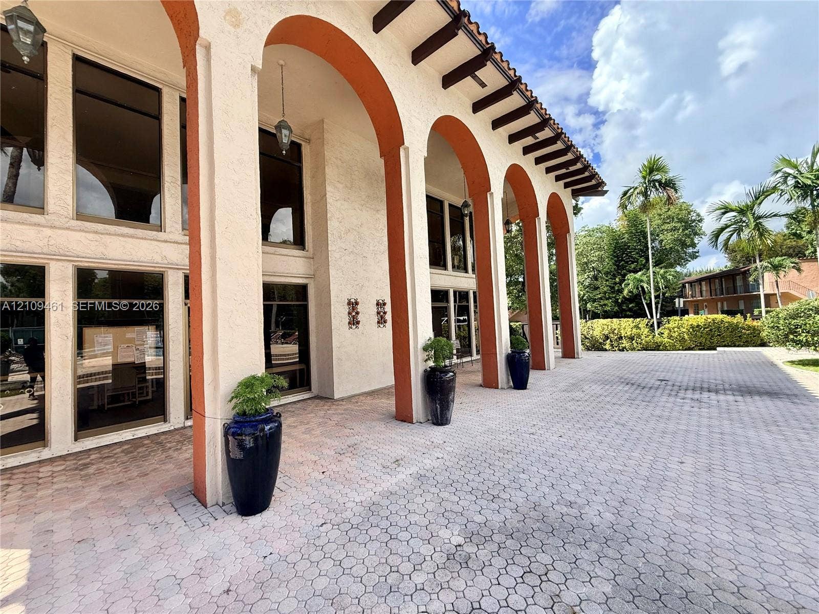 10776 N Kendall Drive, #F11, Miami, FL 33176 Stucco exterior featuring decorative arched colonnades, multi-pane floor-to-ceiling windows, exposed timber rafters, and a paved stone courtyard