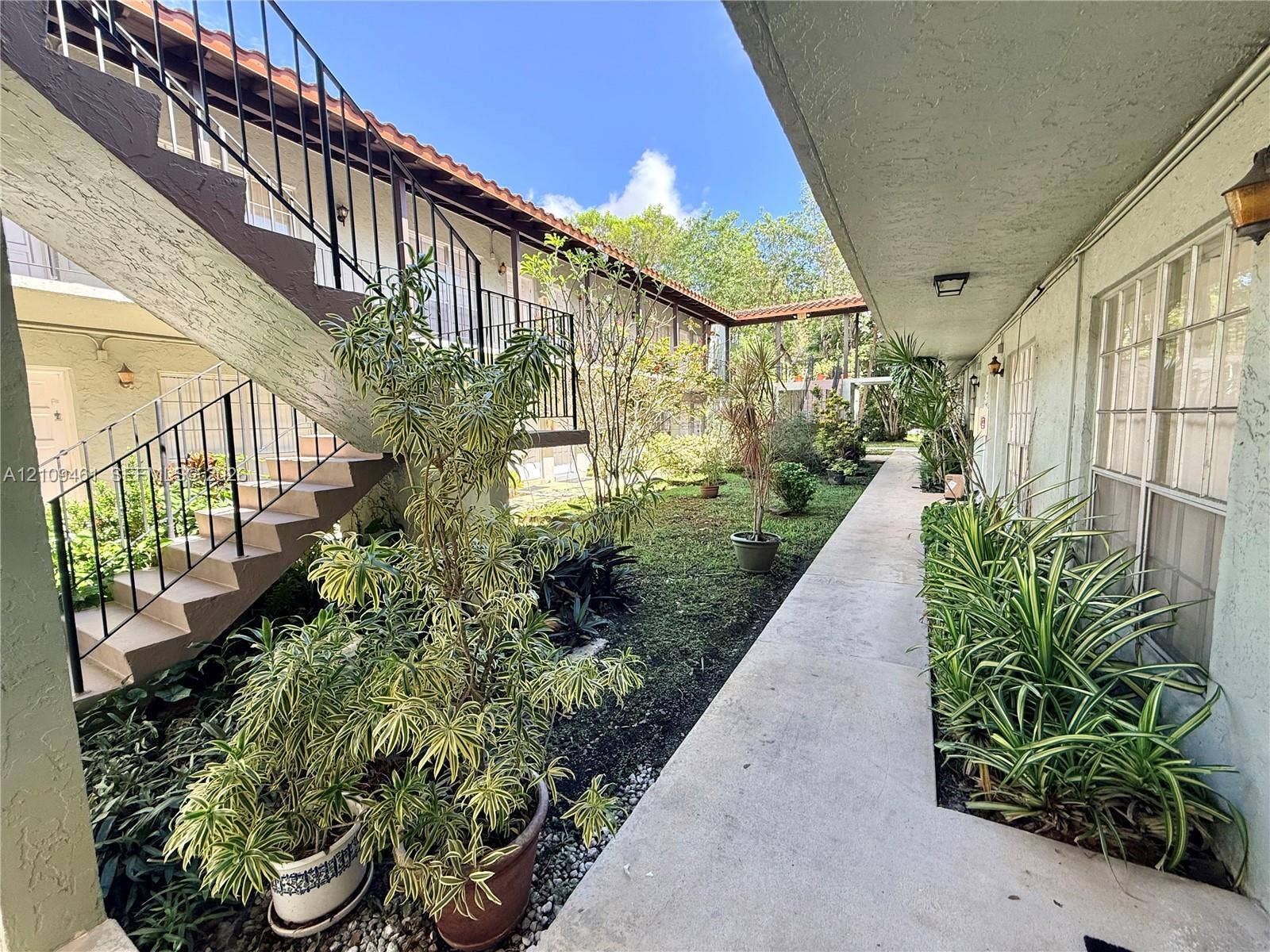 10776 N Kendall Drive, #F11, Miami, FL 33176 Covered exterior walkway with a concrete path, exterior staircase featuring metal railings, and landscaped courtyard area