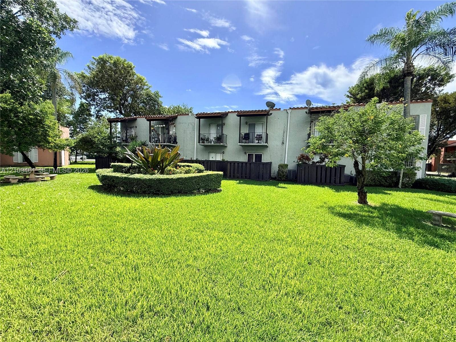 10776 N Kendall Drive, #F11, Miami, FL 33176 Expansive green space featuring mature trees, manicured hedges, building exteriors with terracotta-style roof accents, and private balconies