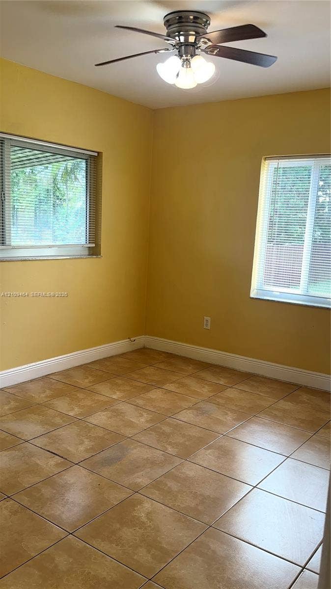 Room interior featuring neutral tile flooring, two windows with horizontal blinds, and a multi-light ceiling fan