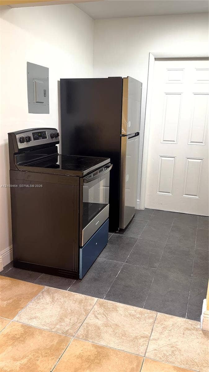 Kitchen featuring a stainless steel and black electric range, a stainless steel refrigerator, dark tile flooring, and a six-panel door