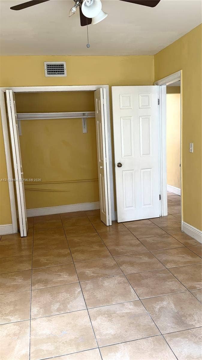 Tile flooring, bi-fold closet doors, interior six-panel door, and a ceiling-mounted fan/light