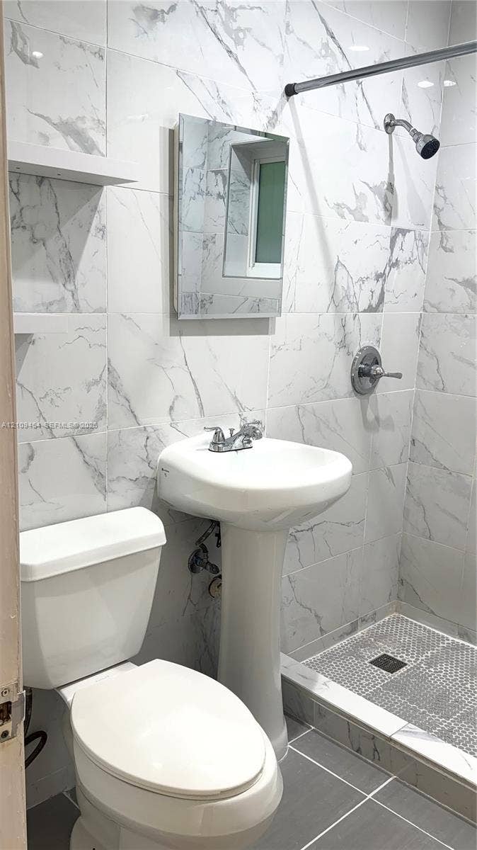 Full-height stone-finish wall tile, pedestal sink, wall-mounted medicine cabinet, built-in shelving, and walk-in shower with tiled flooring
