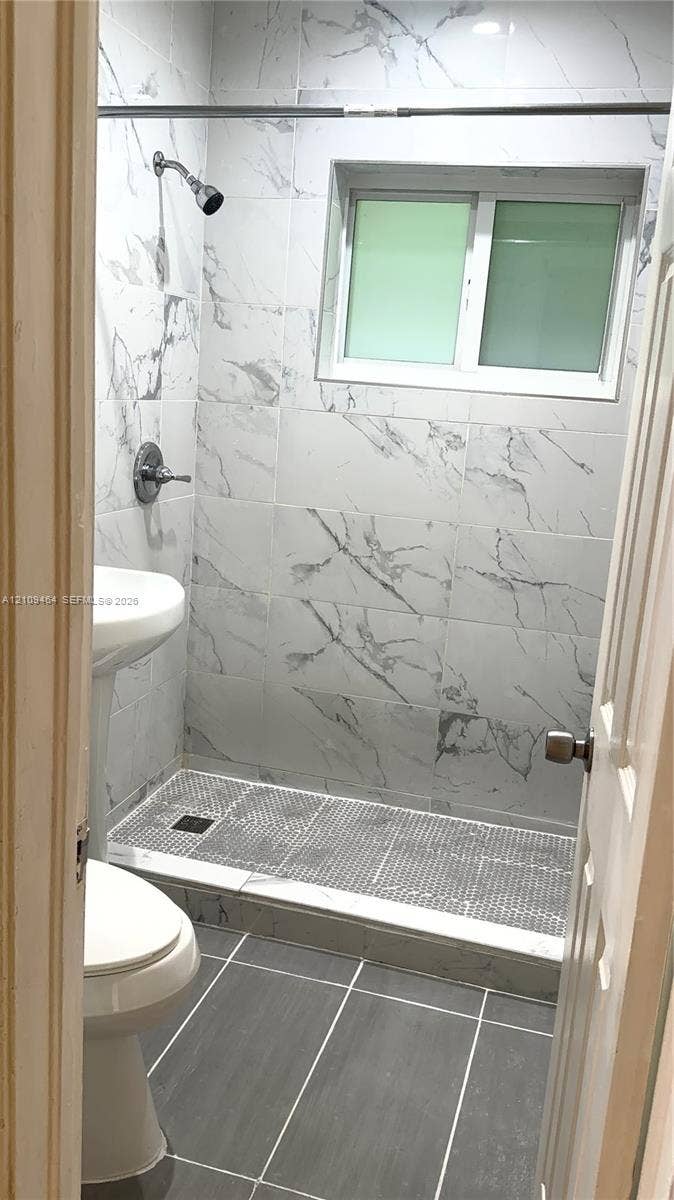 Walk-in shower featuring floor-to-ceiling stone-look tile, a mosaic-tiled shower floor, a white pedestal sink, and large-format grey tile flooring
