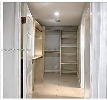 Walk-in closet featuring light-toned tile flooring, built-in open shelving units, and integrated hanging rods