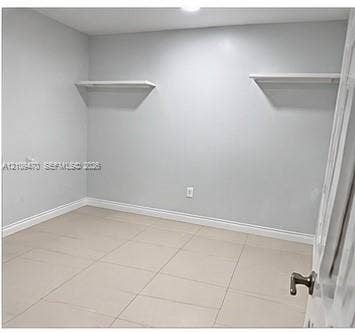 Room featuring neutral-toned tile flooring, light gray walls, and dual built-in wall-mounted shelves