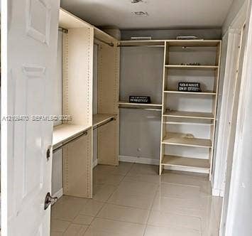 Walk-in closet featuring light-toned custom shelving, multiple hanging rods, and large-format tile flooring