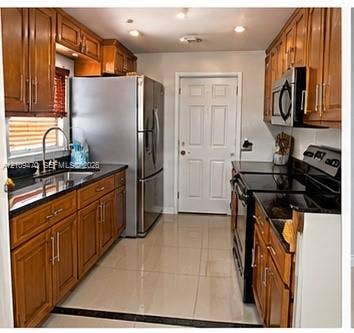 Kitchen featuring stained wood cabinetry, dark stone countertops, stainless steel appliances, recessed lighting, and tile flooring