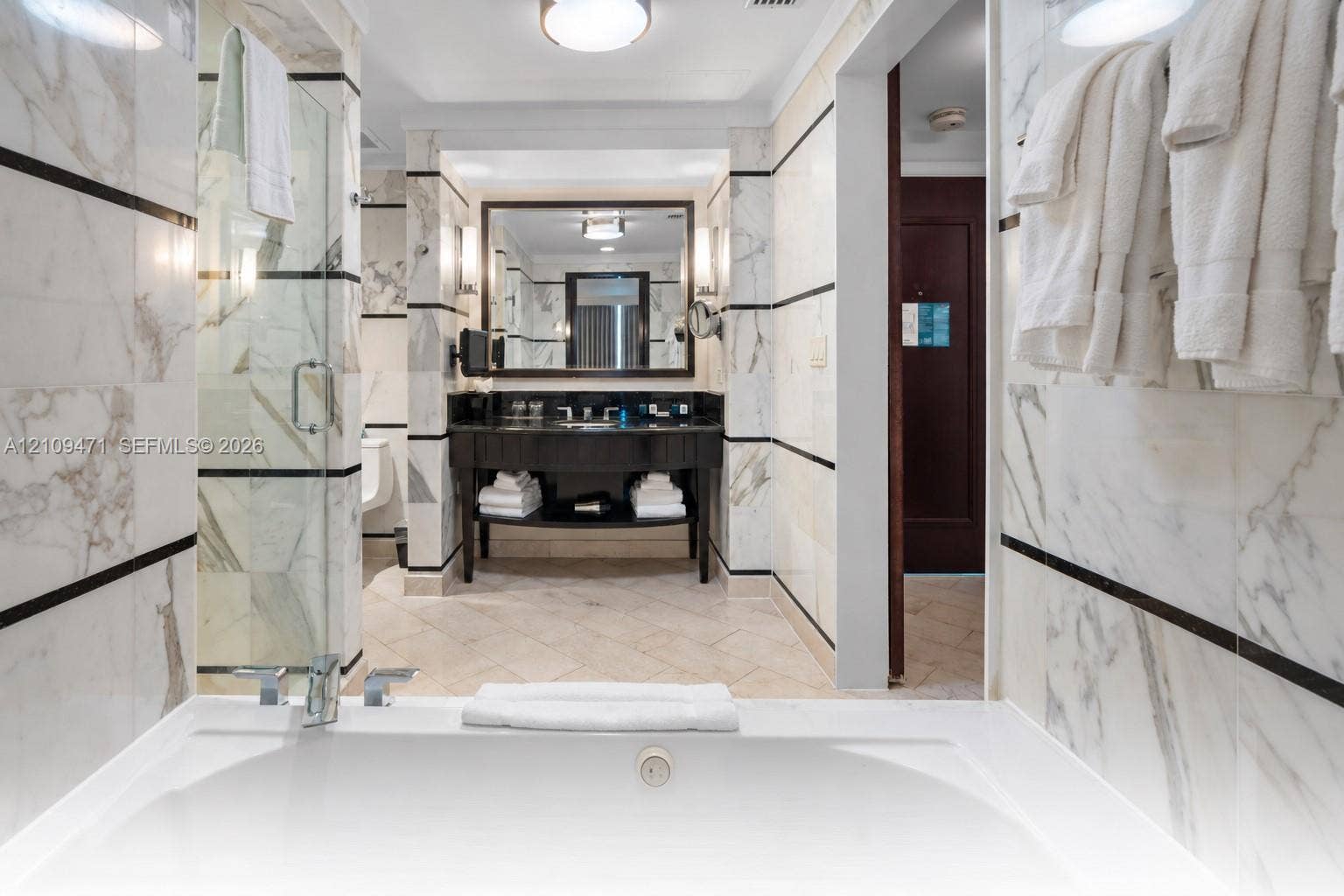 Stone-surround soaking tub, glass-enclosed shower, stone-tiled walls with decorative inlay, dark-finish vanity with countertop sink, and recessed lighting