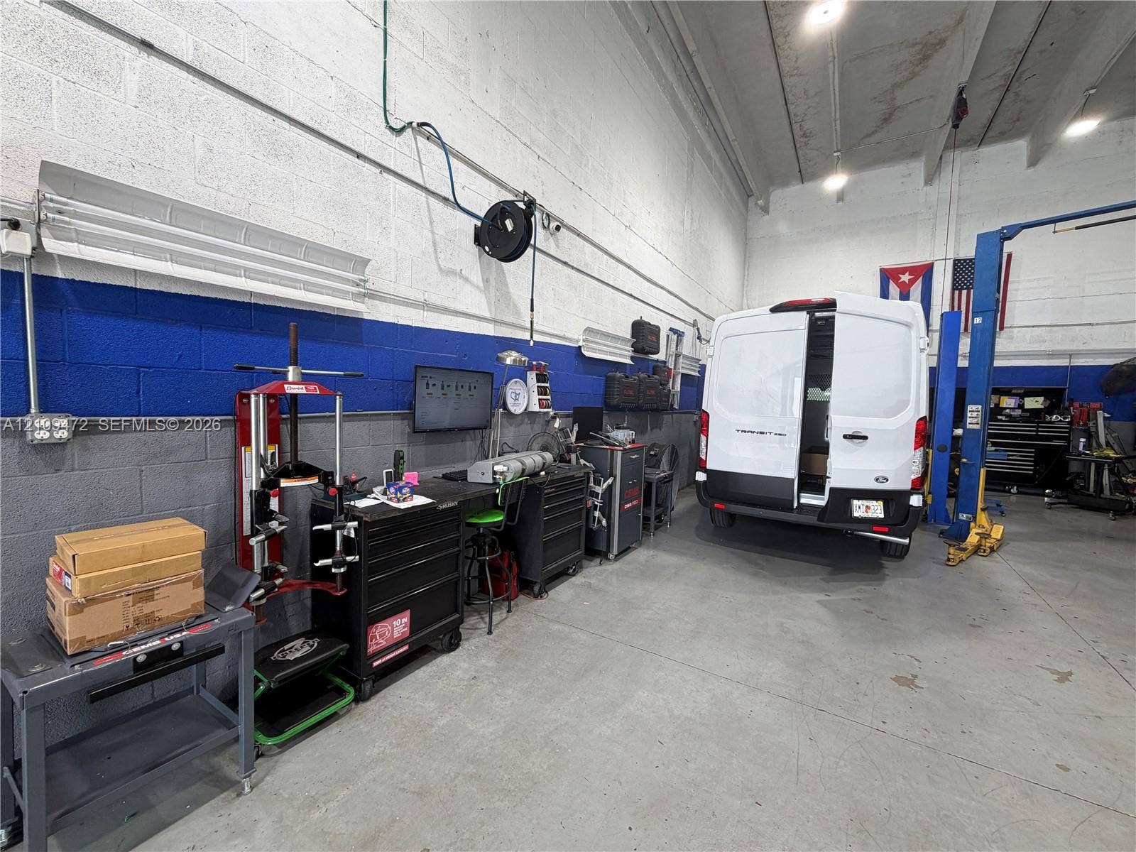 Industrial workspace featuring high ceilings, concrete flooring, painted masonry walls, and a built-in automotive lift