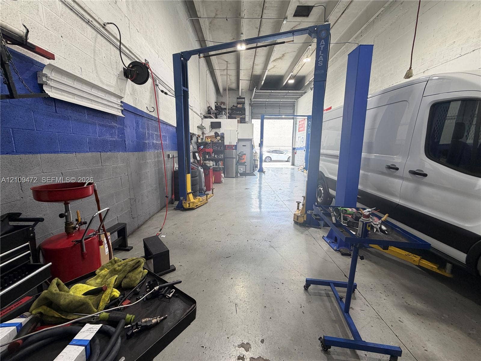 Industrial workshop space featuring concrete flooring, high ceilings with exposed structural elements, and a two-post automotive lift
