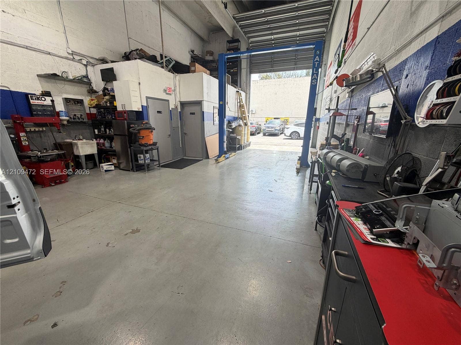 Industrial workspace featuring high ceilings, concrete flooring, dual entry doors, and a built-in automotive lift system