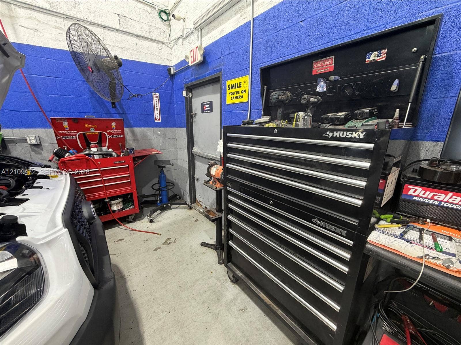 Concrete flooring, painted masonry walls, and wall-mounted industrial fan