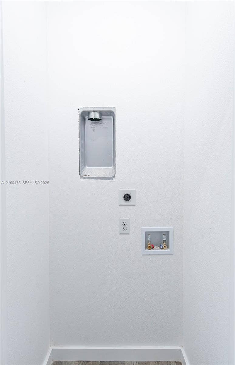 Utility hookup area featuring a recessed dryer vent box, dedicated 240-volt electrical outlet, standard electrical receptacle, and a recessed water supply valve box