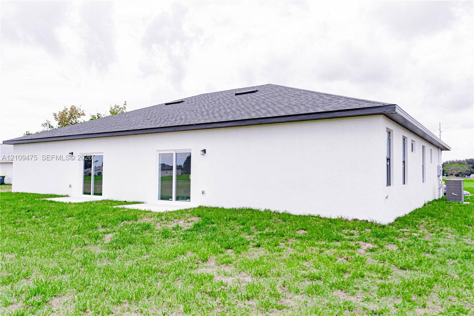 Stucco exterior featuring dual sliding glass doors, a hipped roof with skylights, and concrete patio pads