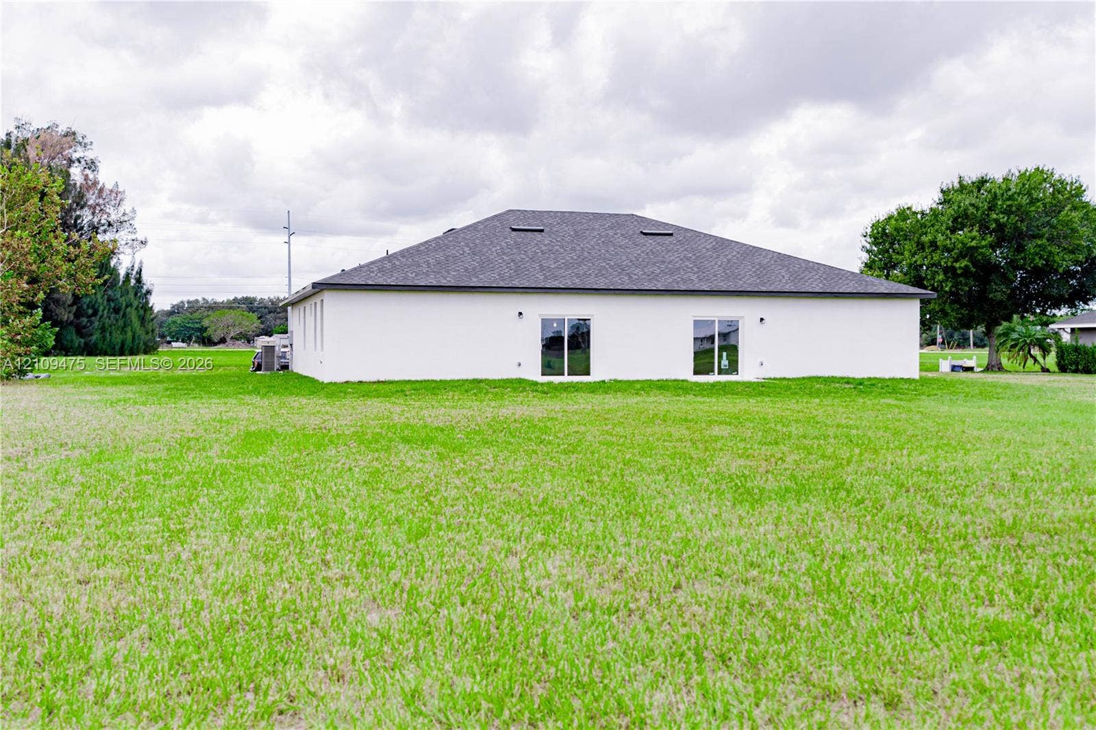 Rear exterior featuring a hip roof, stucco siding, dual glass sliding doors, and a spacious lawn