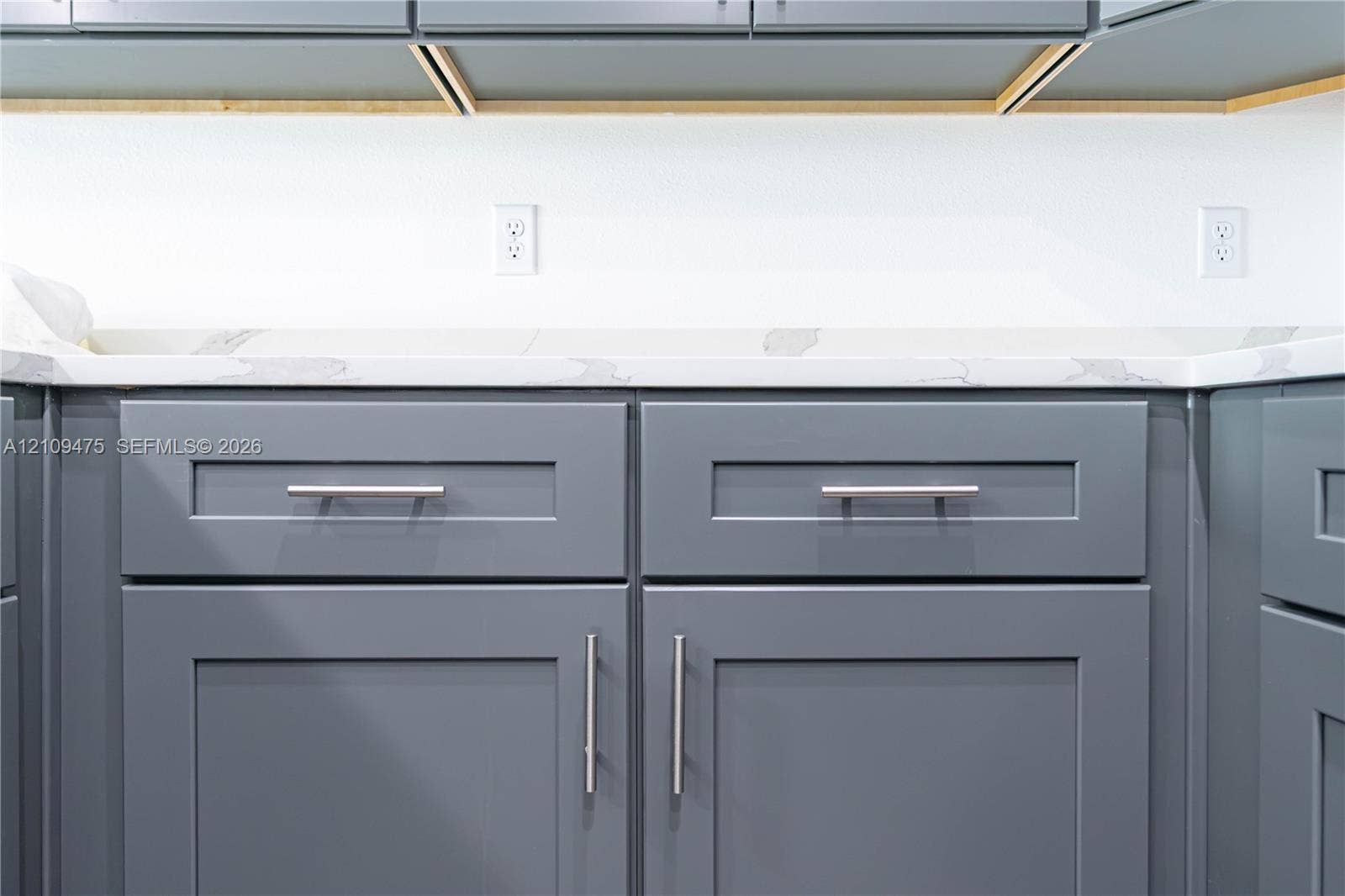 Shaker-style cabinetry finished in a slate grey tone, paired with a white stone-composite countertop featuring grey veining and brushed nickel hardware